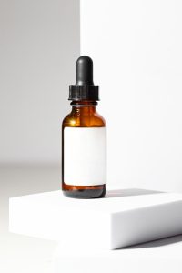 Aesthetic cosmetic  background. Dropper bottle with black pipette and whita label on white podium. Beauty product and skin care cocnept
